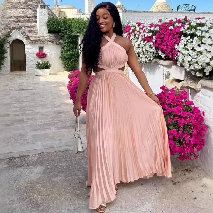 Robe longue plissée rose poudré en satin pour femme, style africain élégant, avec découpes à la taille, sans manches, pour soirée ou événement.